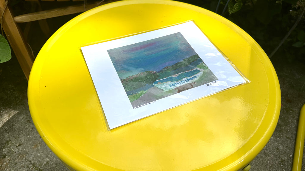 An art print featuring a colorful landscape painting of a swimming pool, displayed on a bright yellow outdoor table.